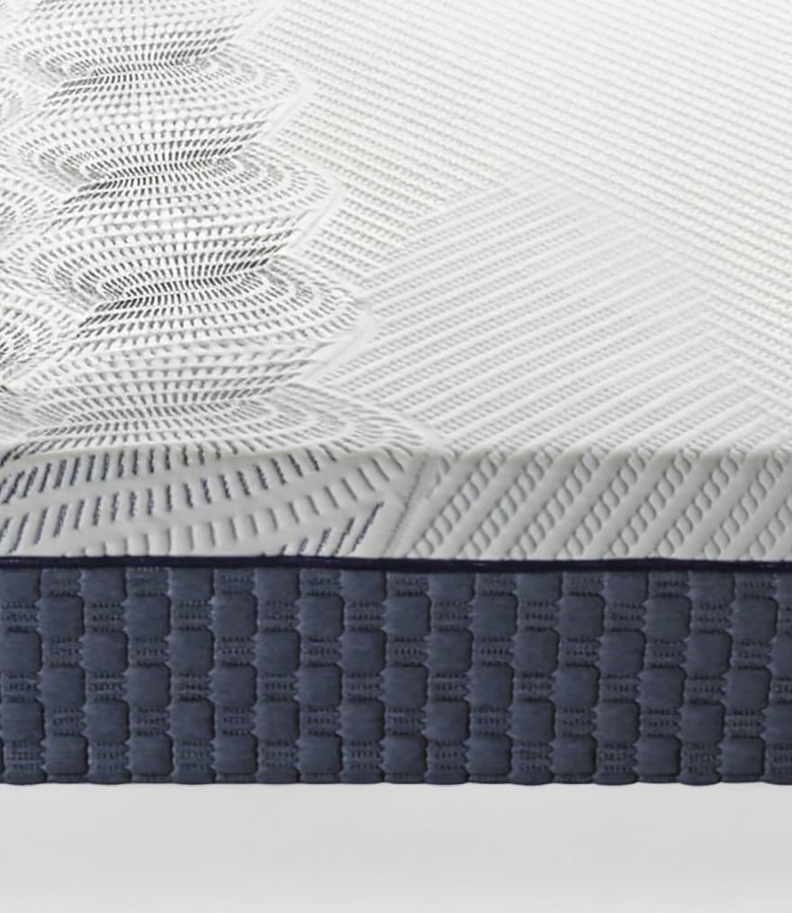 Superficie di materasso bianco con motivi geometrici e bordo inferiore imbottito grigio scuro a trama regolare.