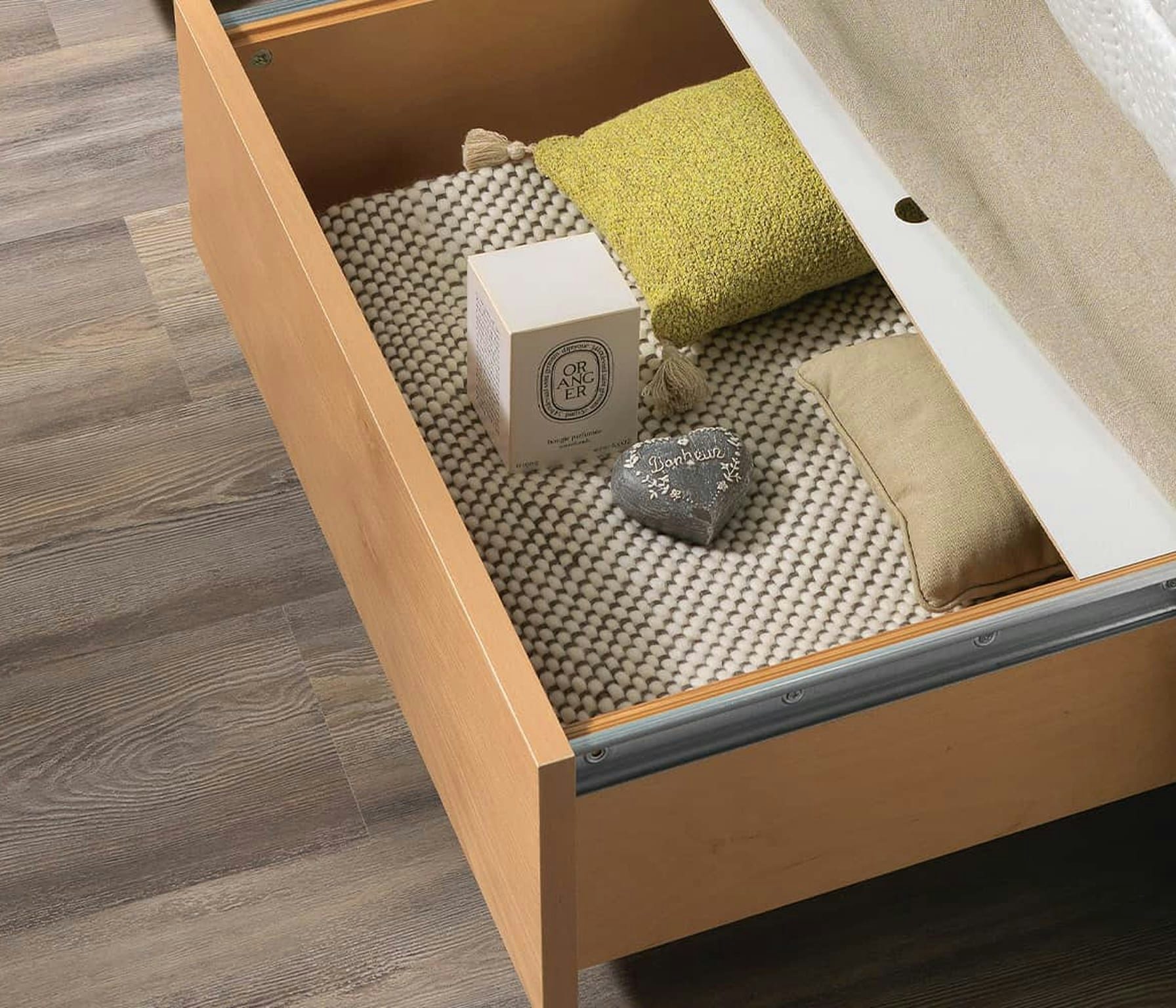 Cassetto di legno aperto con tappeto a trama grossa bianco e grigio, due cuscini e un cuore decorativo con scritta bonheur