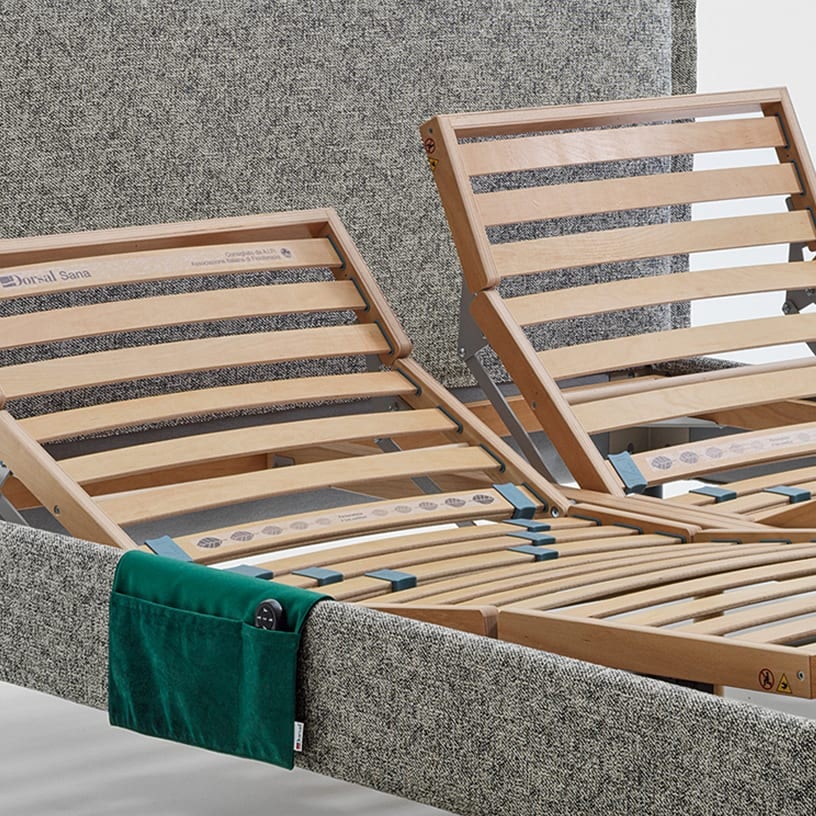 Rete letto regolabile in legno con struttura imbottita grigia e tasca porta telecomando verde.