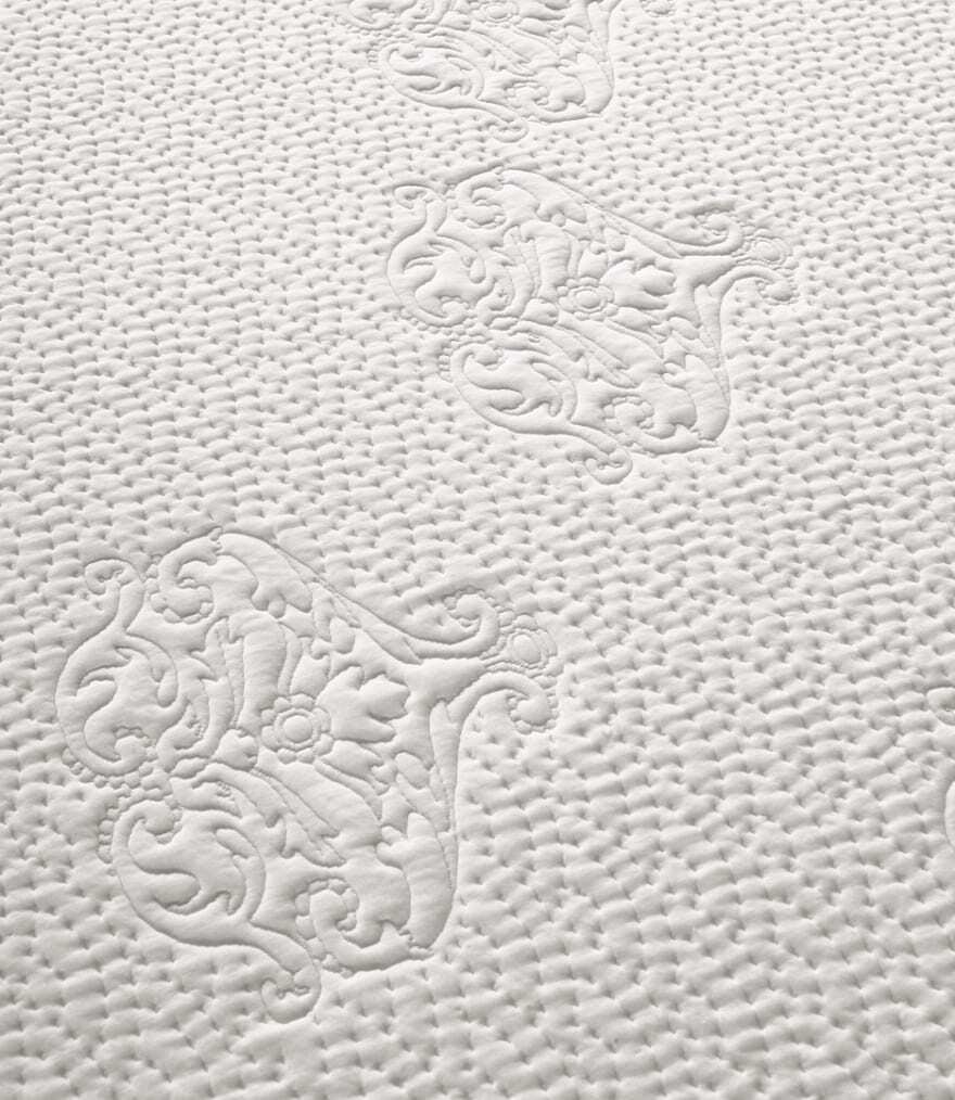 Texture bianca trapuntata con motivi floreali in rilievo e fondo a piccoli puntini concentrici.