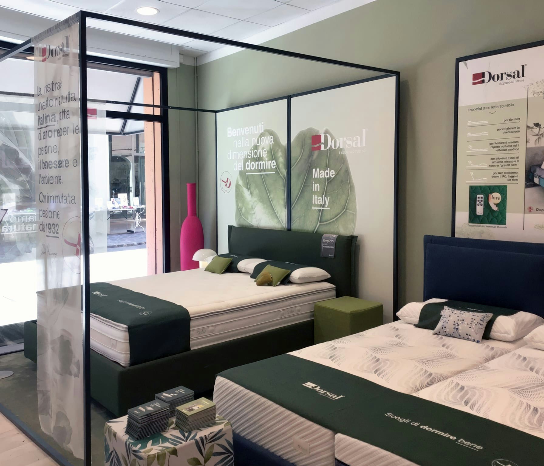 Due letti matrimoniali con testiere imbottite in esposizione in negozio Dorsal Made in Italy, con decorazioni verdi e…