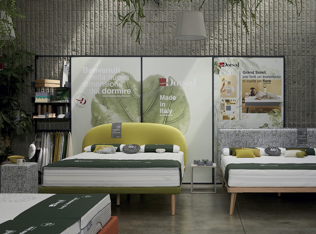 Letti con testiere imbottite in esposizione in showroom con sfondo pubblicitario Dorsal Made in Italy.