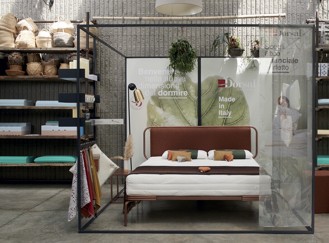 Letto matrimoniale con testiera marrone, cuscini colorati e mensole con tessuti e ceste di arredamento su sfondo muro a…