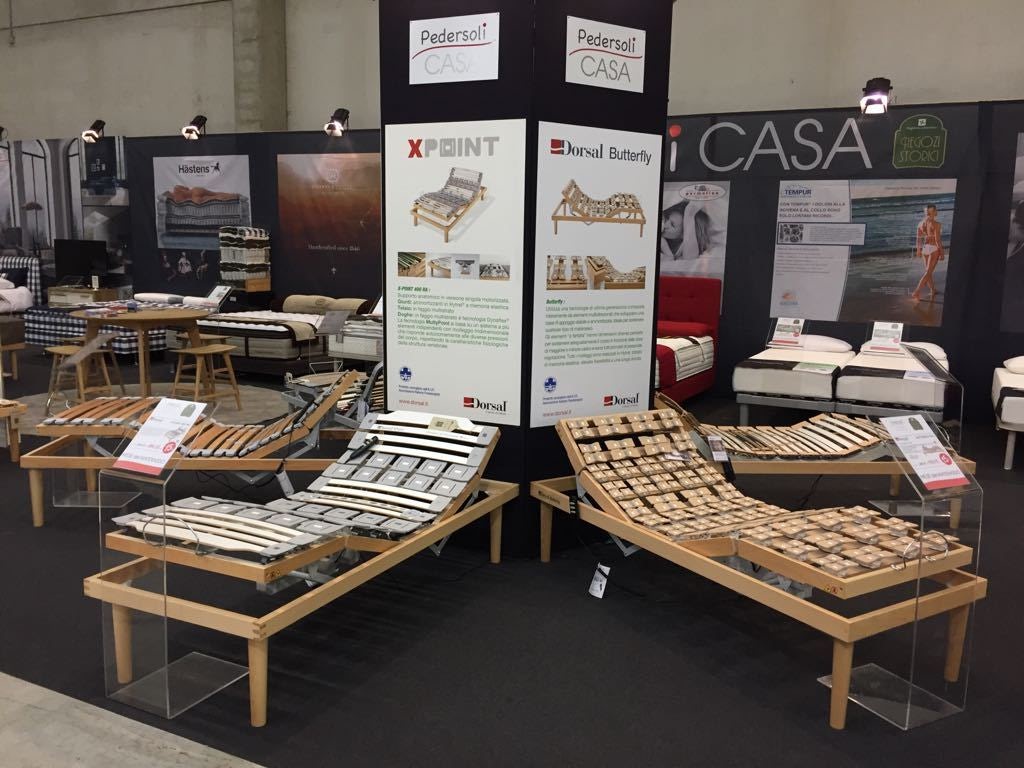 Reti letto regolabili Pedersoli Casa esposte in fiera con dettagli costruttivi e brochure informative visibili.