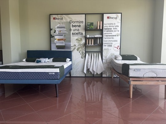 Due letti matrimoniali con materassi e cuscini in esposizione, dietro due pannelli con testo promozionale Dorsal.