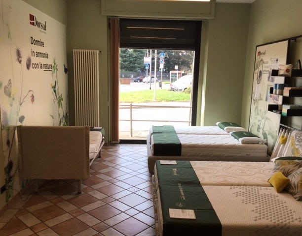 Showroom con materassi esposti, parete decorata con fiori e testo Dormire in armonia con la natura, ampio finestrone su…