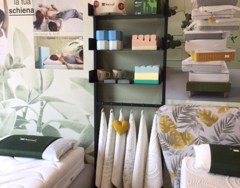 Esposizione prodotti per il riposo Dorsal con materassi, cuscini, asciugamani e box espositivo con logo rosso e nero.