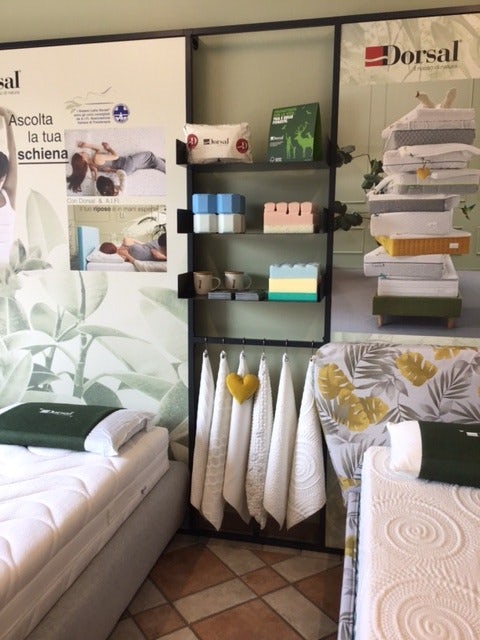 Esposizione prodotti per il riposo Dorsal con materassi, cuscini, asciugamani e box espositivo con logo rosso e nero.