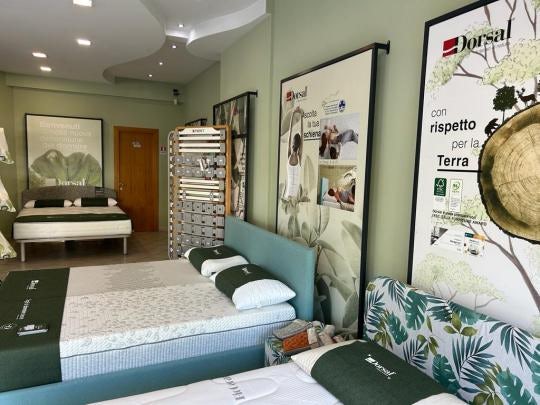 Negozio con letti e materassi Dorsal esposti in stanza con pareti color verde salvia e manifesti promozionali.