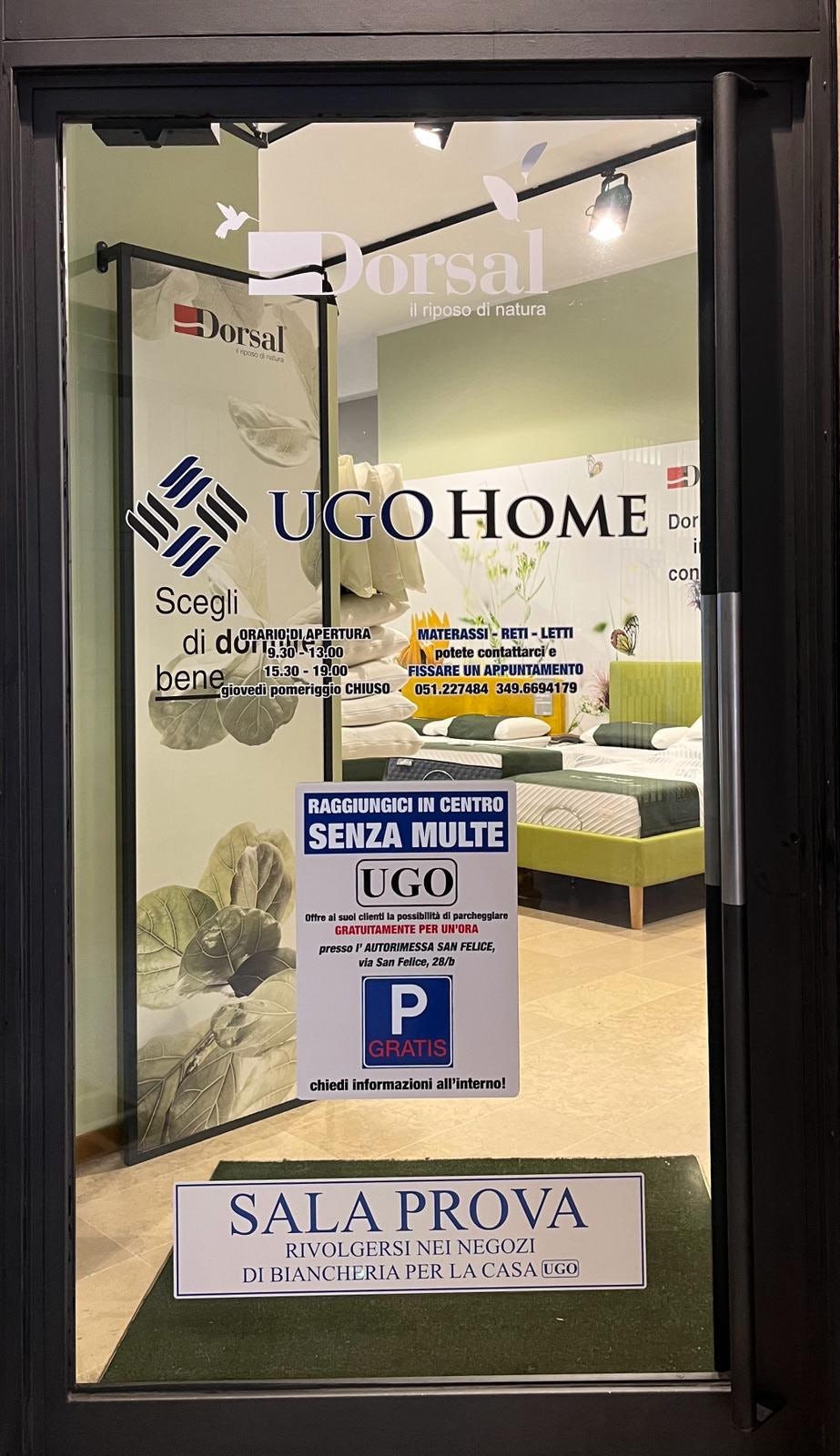 Vetrina con logo UGO HOME, orari di apertura, offerta parcheggio gratis e indicazione sala prova biancheria per la casa.