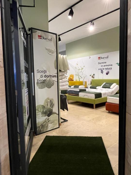 Ingresso di negozio con letti esposti, pannelli pubblicitari Dorsal con testi su sonno e natura, pareti verdi e pavimento…