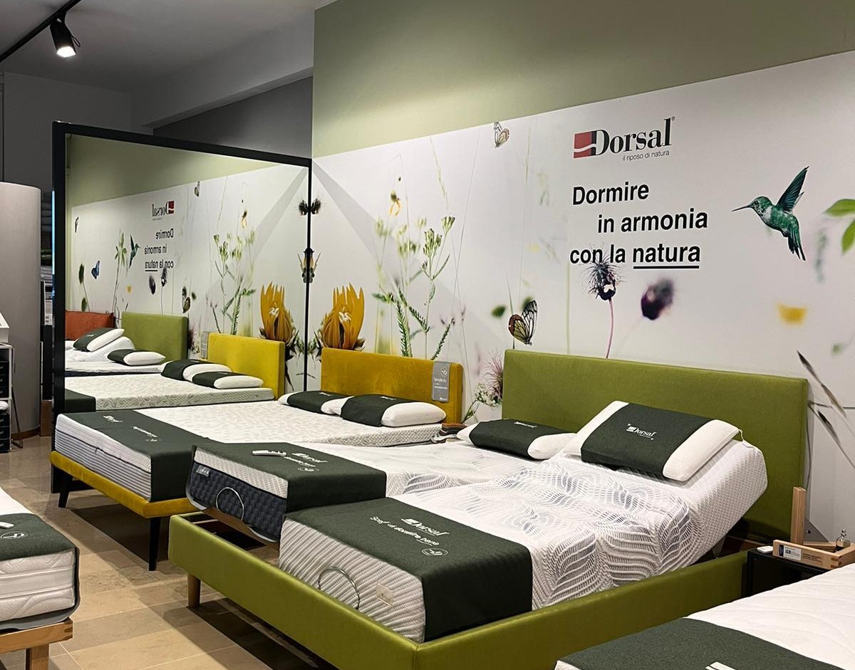 Letti matrimoniali con testiera colorata in esposizione in negozio di arredamento, parete decorata con fiori e colibrì.