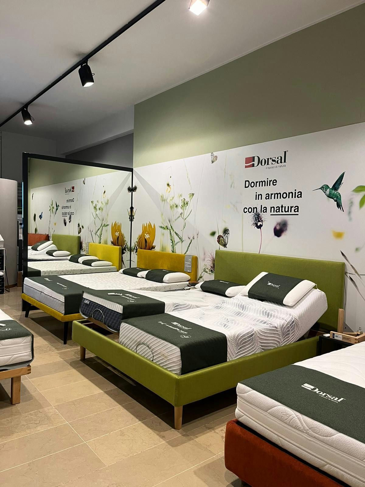 Letti matrimoniali con testiera colorata in esposizione in negozio di arredamento, parete decorata con fiori e colibrì.