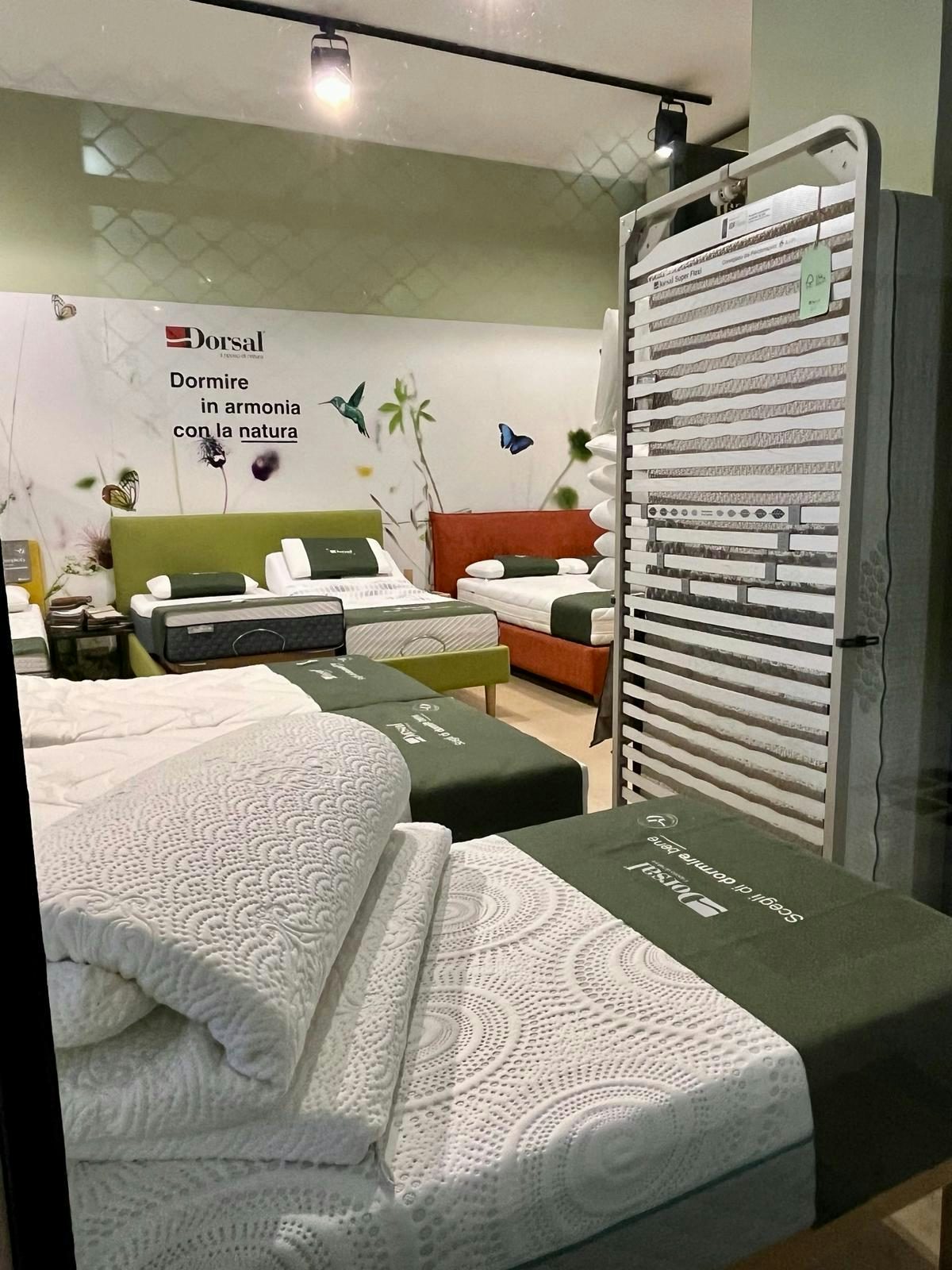 Letti esposti con materassi e coperte imbottite in showroom arredato con decorazioni naturali e scritta Dormire in armonia…