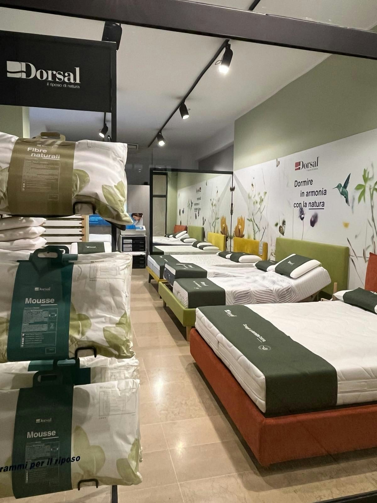 Negozio con diversi letti e cuscini Dorsal, parete decorata con slogan Dormire in armonia con la natura.