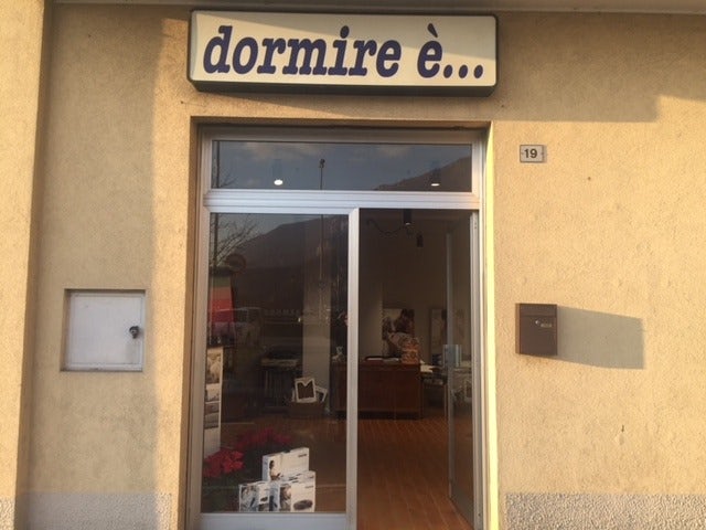 Ingresso di un negozio con vetrina e insegna sopra con scritto dormire è... numero civico 19 e cassetta postale marrone.