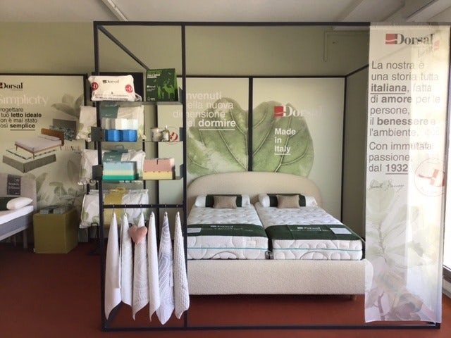 Letto matrimoniale con due materassi, scaffale con asciugamani e prodotti, sfondo con foglie e scritte in italiano.