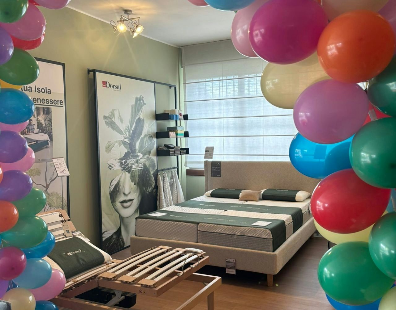 Arco di palloncini colorati in negozio con letti e materassi esposti su pavimento in legno.