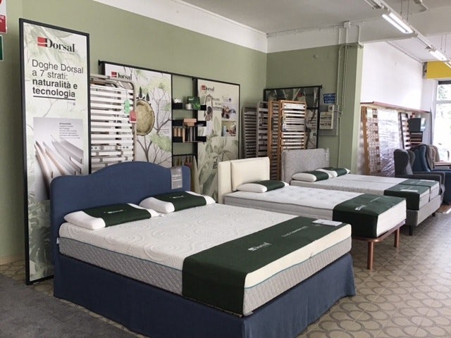 Esposizione di letti singoli e matrimoniali con materassi bianchi su strutture imbottite e cataloghi Dorsal sullo sfondo.
