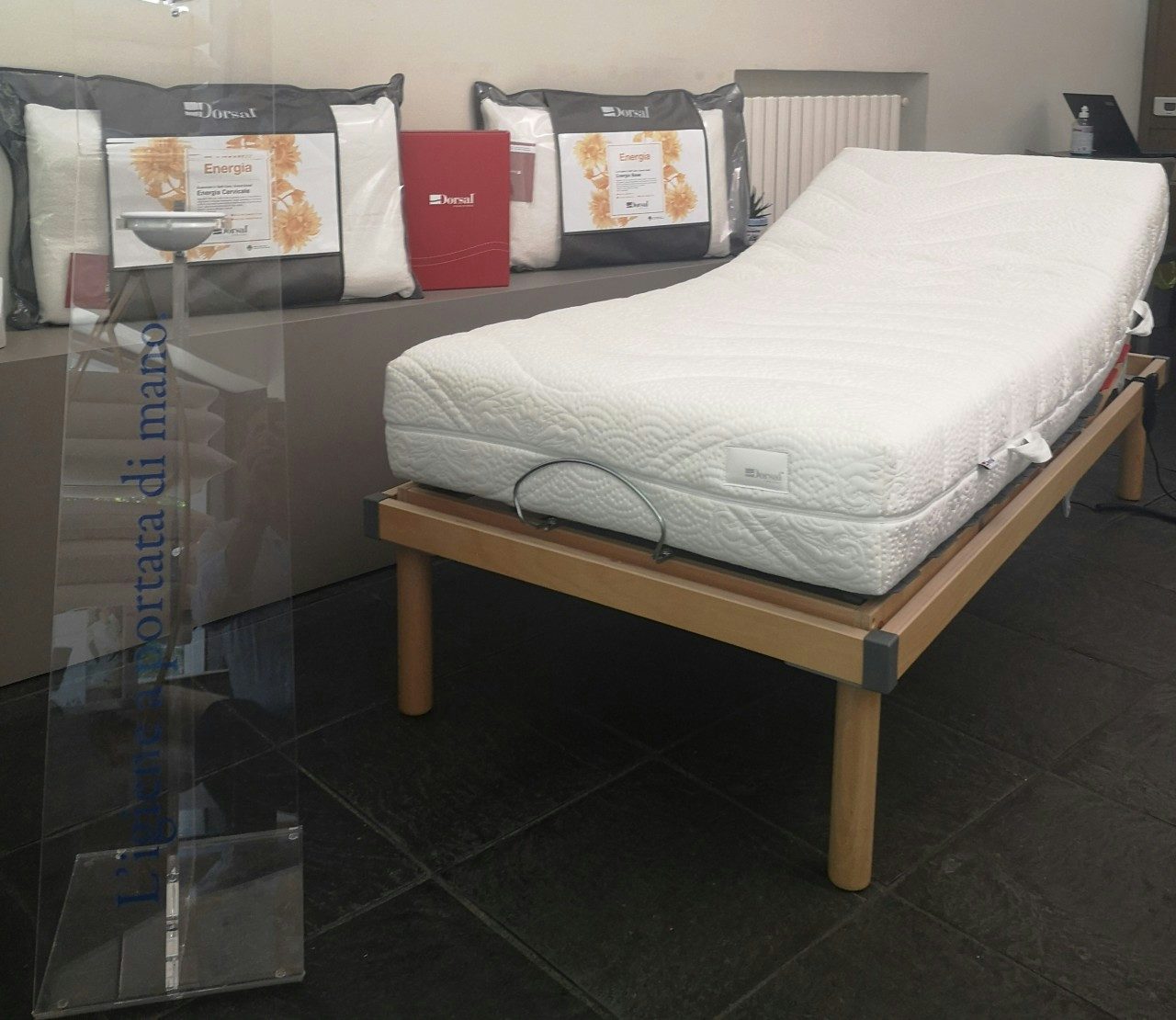 Letto inclinabile con supporto in legno chiaro e materasso bianco imbottito, cuscini da letto e totem trasparente con…