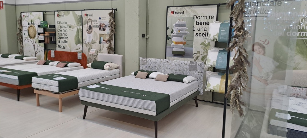Letti con materassi e cuscini verde salvia esposti in negozio specializzato in prodotti per il sonno.