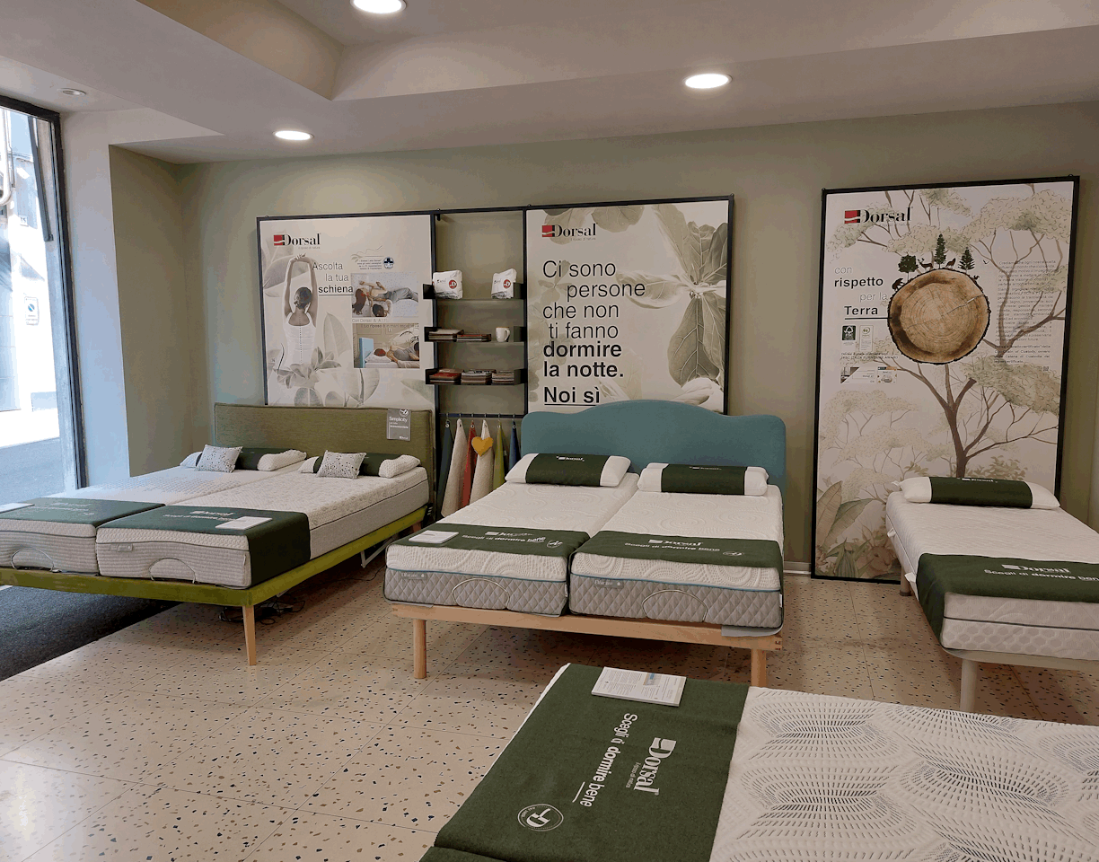 Letti esposti in negozio con materassi e cuscini, pannelli pubblicitari del marchio Dorsal alle spalle.