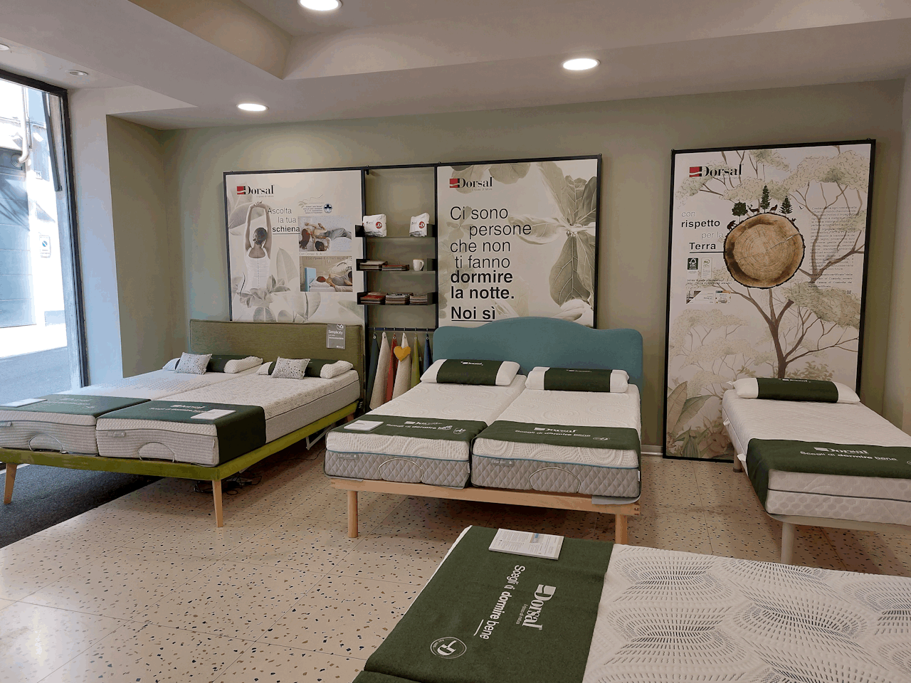 Letti esposti in negozio con materassi e cuscini, pannelli pubblicitari del marchio Dorsal alle spalle.