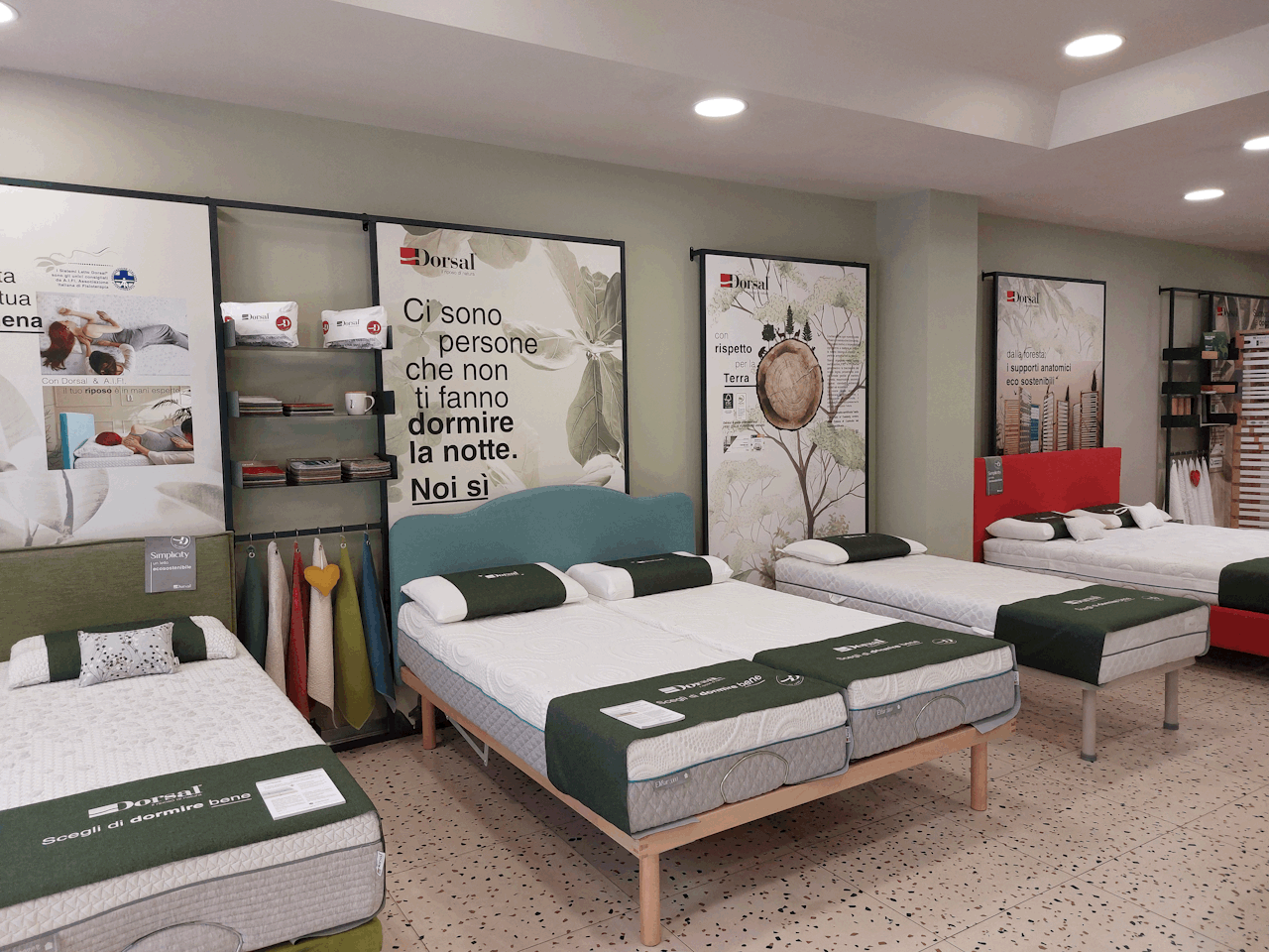 Letti con materassi Dorsal esposti in showroom con cartelloni pubblicitari e campioni di tessuti appesi.