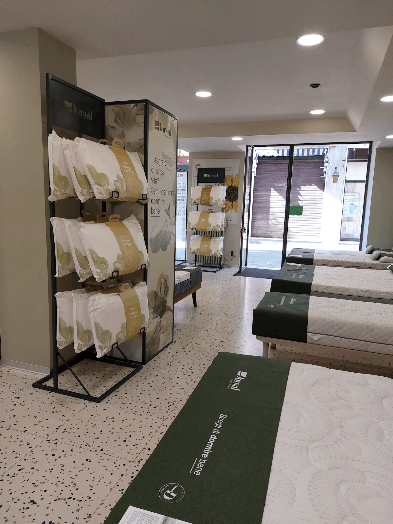Negozio con letti esposti con coprimaterassi verdi e scaffali con cuscini Dorsal energia soft care.