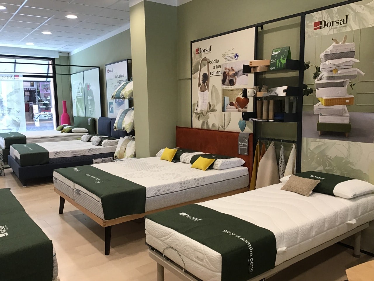 Negozio con materassi e letti in esposizione con coprimaterassi verdi e decorazioni di cuscini gialli e beige.