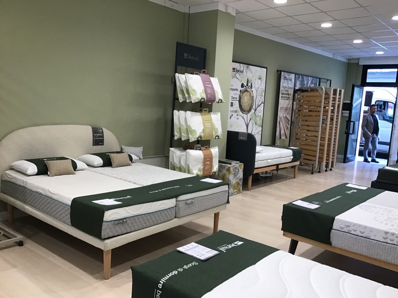 Negozio con letti esposti, cuscini e materassi con coperture verdi, pareti verdi e uomo vicino all'ingresso.
