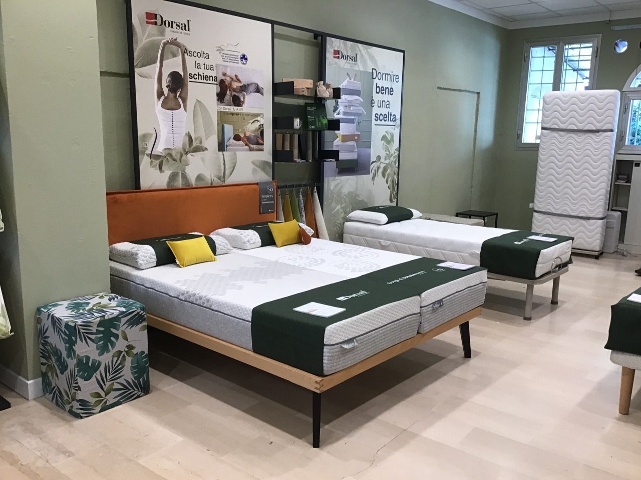 Showroom di materassi e letti con decorazioni verdi, cuscini gialli e poster che promuovono il benessere della schiena.