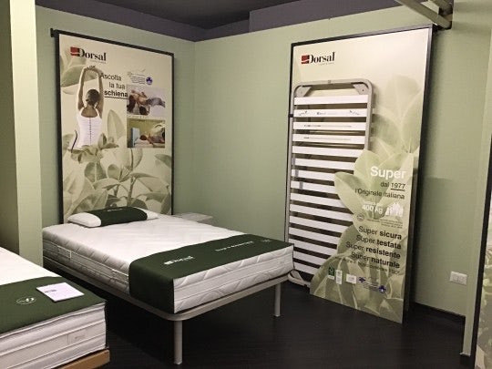 Letto singolo con materasso e supporto a doghe in una stanza con manifesti promozionali Dorsal per la schiena e la sicurezza…