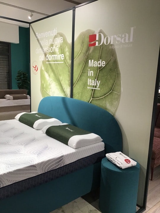 Letto matrimoniale con testiera turchese, due cuscini ergonomici e scritta Benvenuti nella nuova dimensione del dormire…