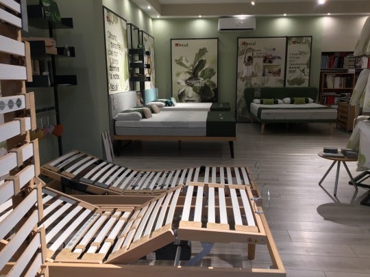 Negozio con letti e materassi, struttura in legno a doghe regolabili in primo piano, poster e scaffali sullo sfondo.