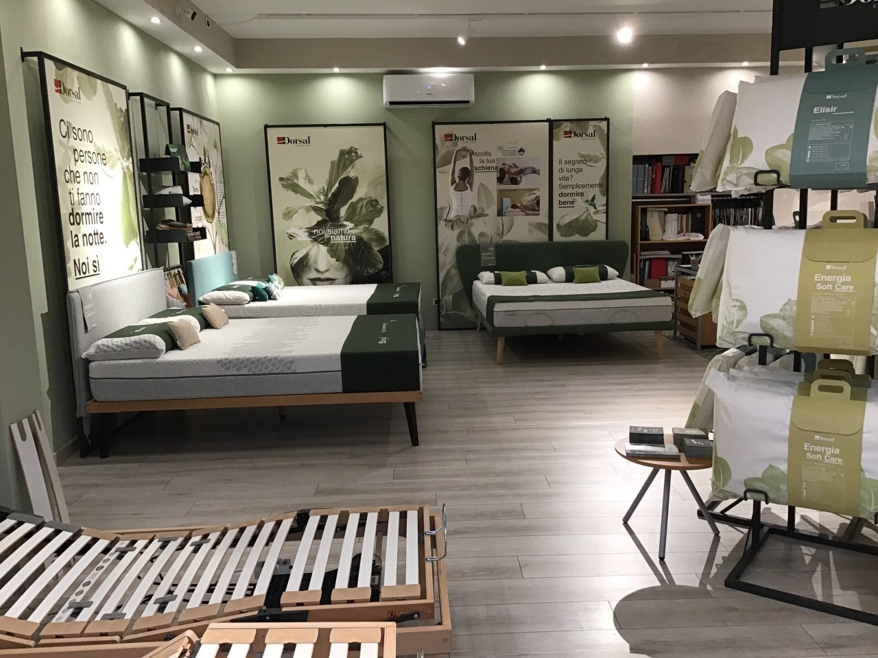 Negozio con tre letti matrimoniali con materassi e una struttura in legno per reti regolabili, esposizione di cuscini con…