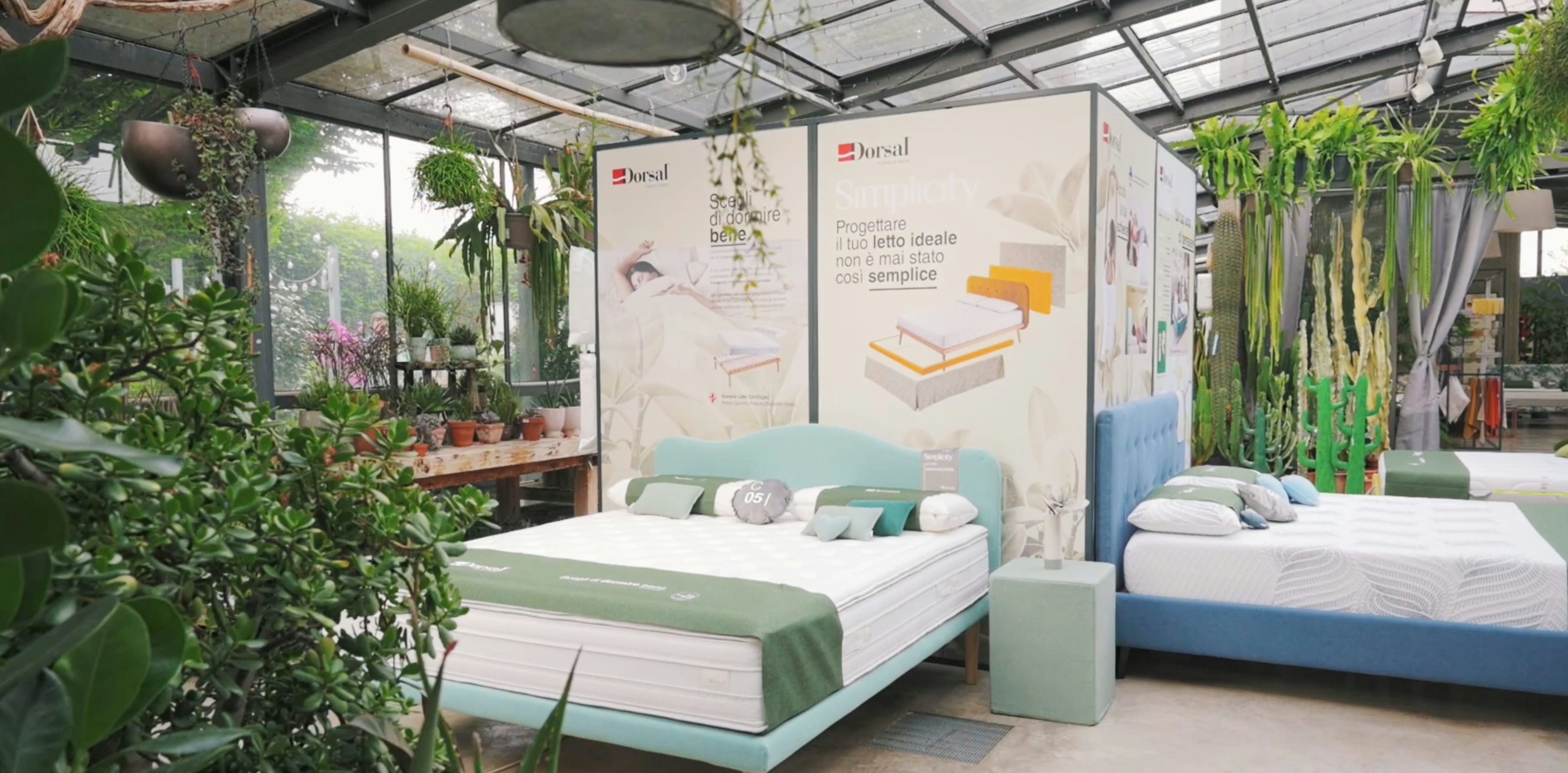 Letti moderni con testiere imbottite in esposizione in un negozio luminoso pieno di piante verdi e fiori.