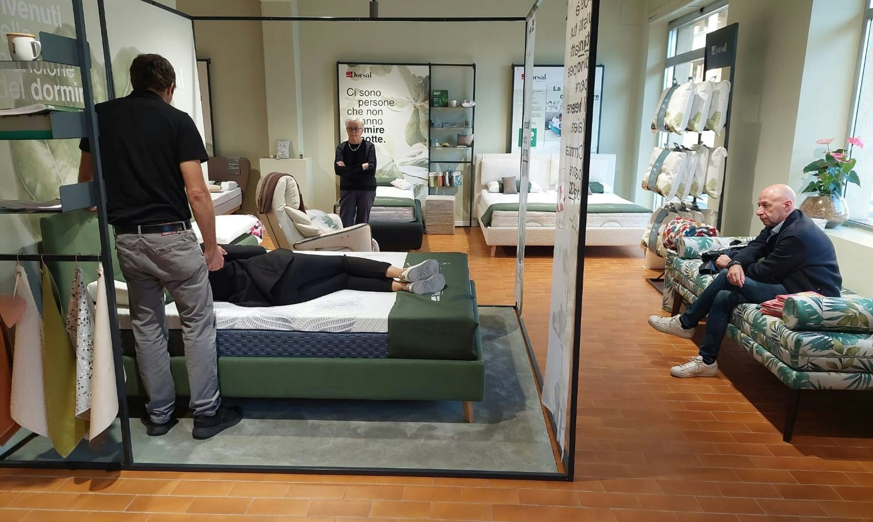 Negozio arredamento con persone che provano materassi e divani, pavimento in cotto e vetrina luminosa.