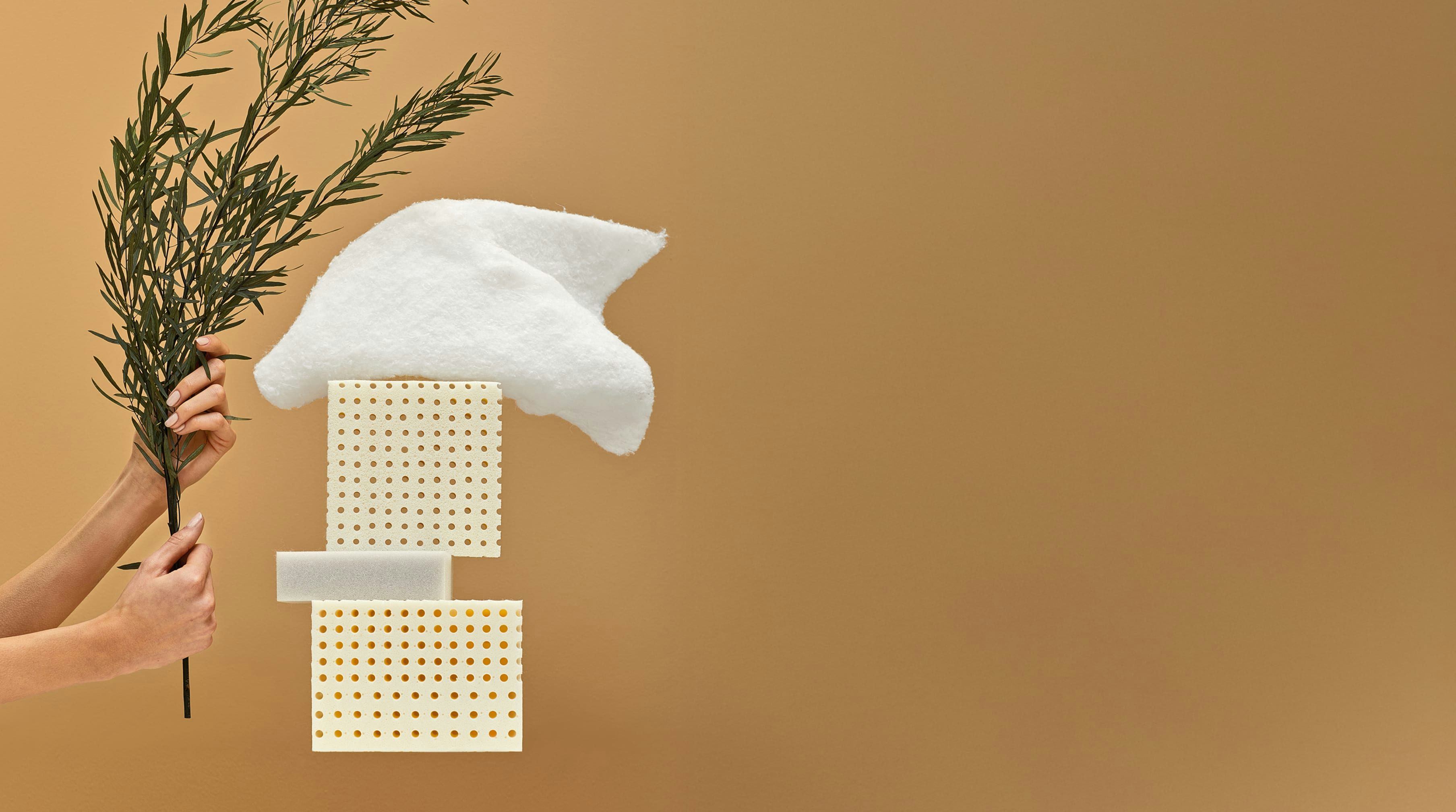 Mani che tengono un ramo verde accanto a tre blocchi di materiale e un pezzo di tessuto bianco su sfondo marrone chiaro.