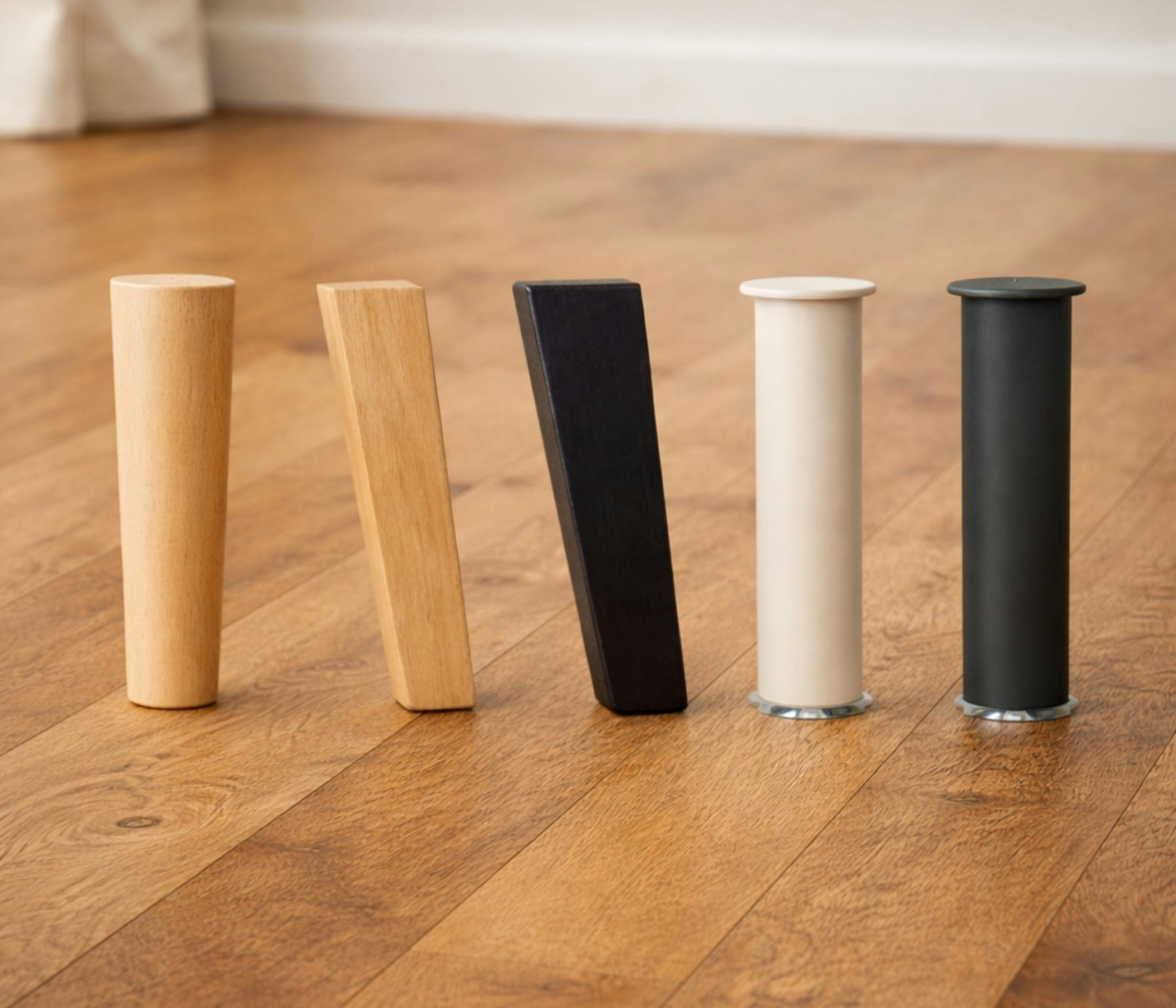 Cinque gambe di mobili di diverse forme e colori, da legno chiaro a nero, su pavimento in legno.