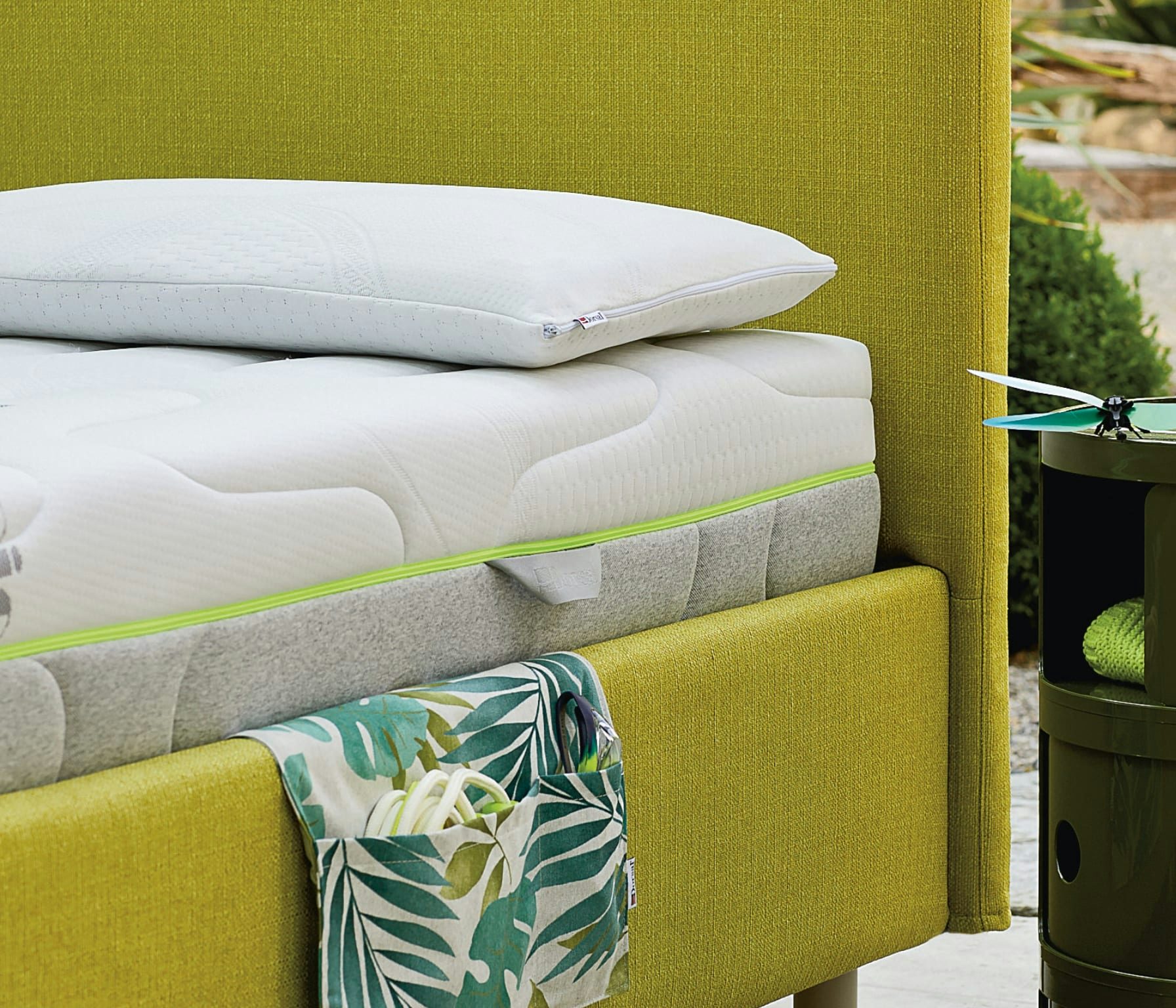 Letto imbottito verde con cuscino bianco, materasso con bordo verde lime e portaoggetti a fantasia foglie.