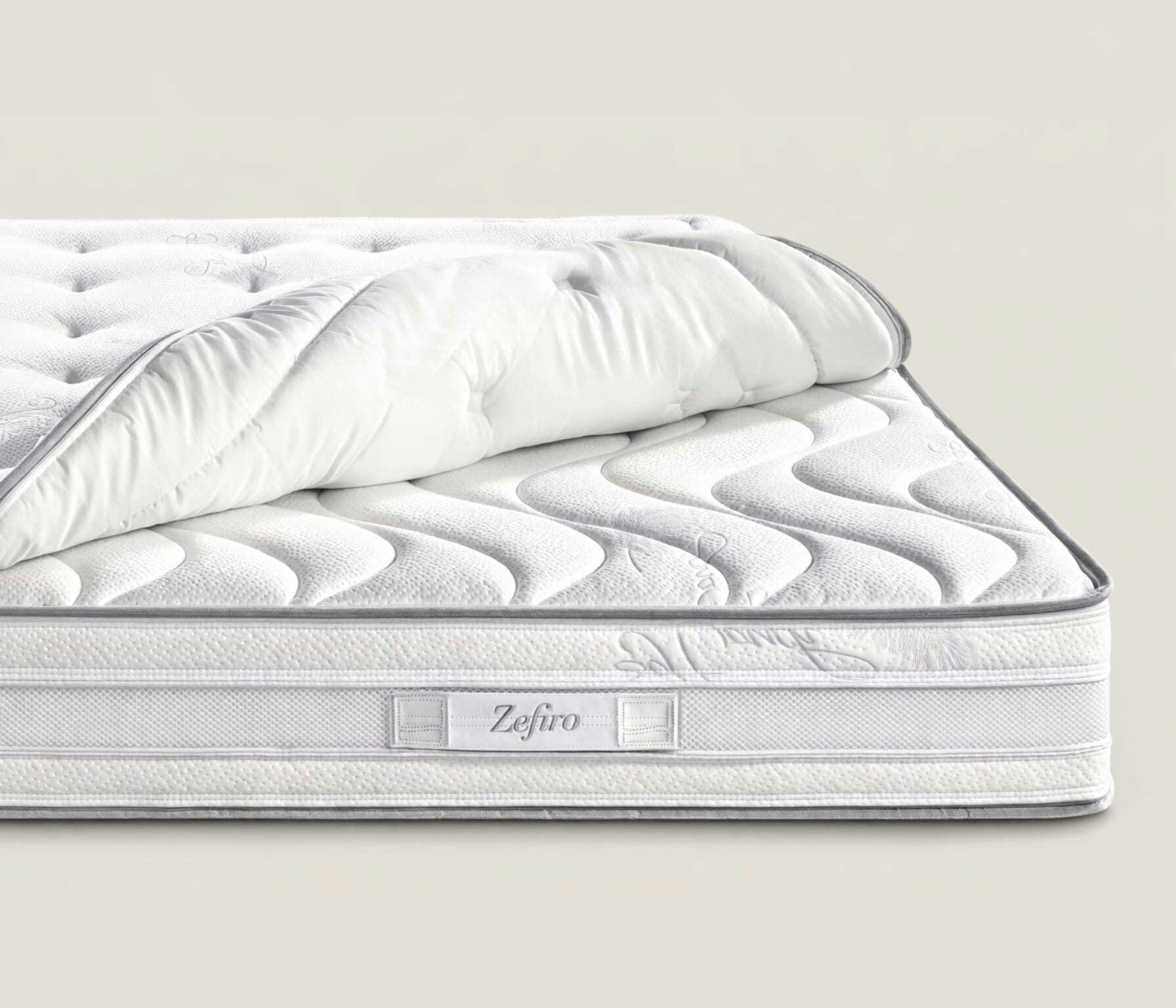 Materasso bianco con superficie trapuntata e logo Zefiro, rivestimento spesso parzialmente sollevato per mostrare…