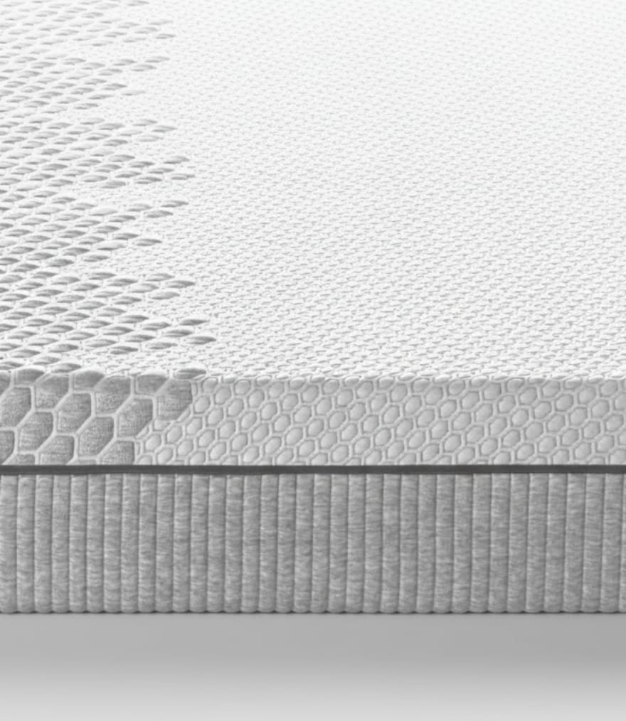 Dettaglio della superficie e del bordo di un materasso grigio con trama a esagoni e inserti a rete traspirante.