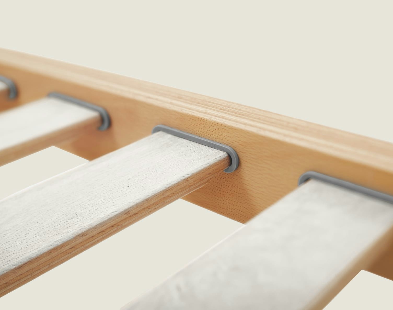 Struttura lettino in legno chiaro con doghe orizzontali bianche inserite e supporti grigi in plastica.