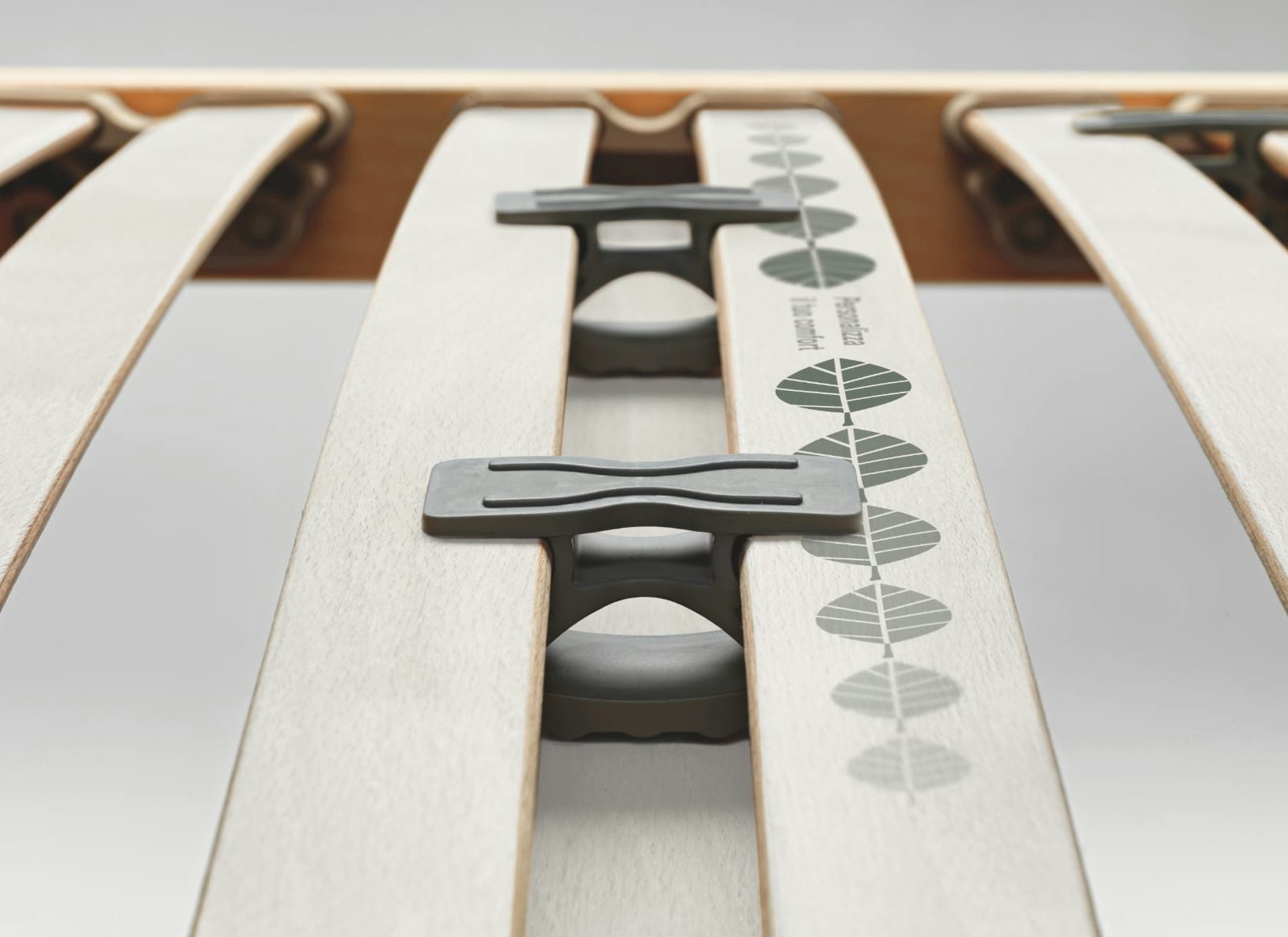 Particolare di una rete letto in legno con supporti grigi e decorazione a foglie sul listello centrale.