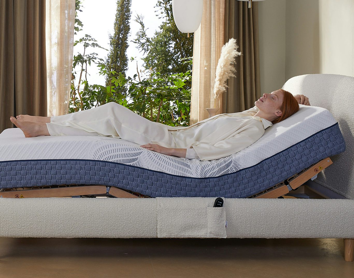 Una donna distesa su un materasso regolabile con uno strato blu. Una pianta è visibile sullo sfondo.