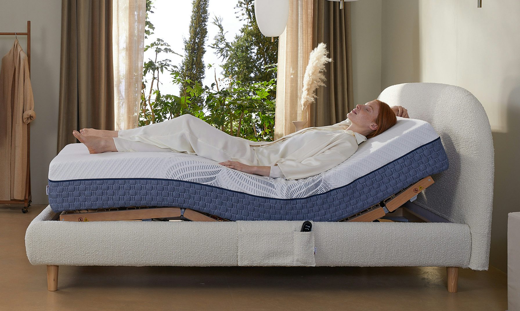 Una donna distesa su un materasso regolabile con uno strato blu. Una pianta è visibile sullo sfondo.