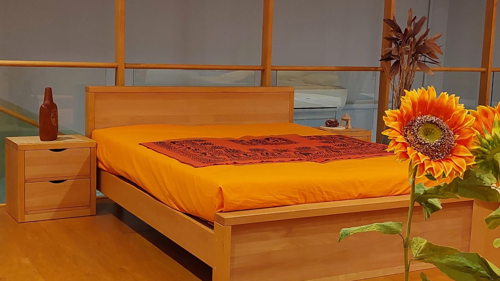 Camera con letto matrimoniale arancione, cuscini bianchi, comodino in legno e decorazioni floreali.