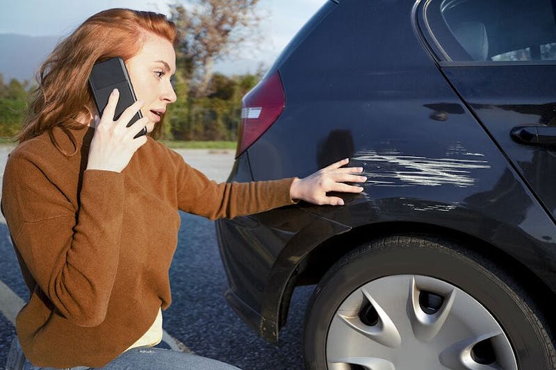 Woman on the phone next to a scratched car