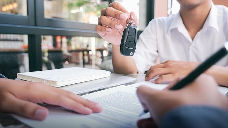person holding their car keys while someone else fills out paperwork